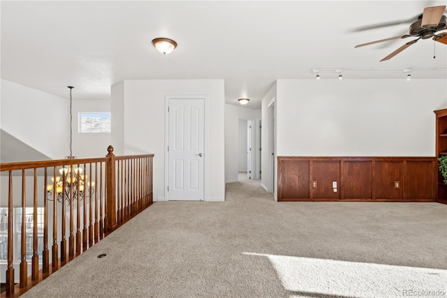 carpeted empty room with ceiling fan with notable chandelier, rail lighting, and wooden walls