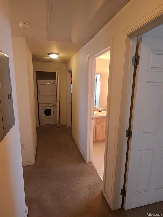 corridor featuring stacked washer / drying machine, baseboards, and a sink