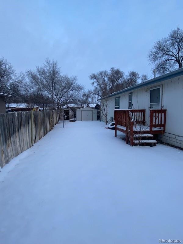 snowy yard featuring a garage, an outdoor structure, and a wooden deck