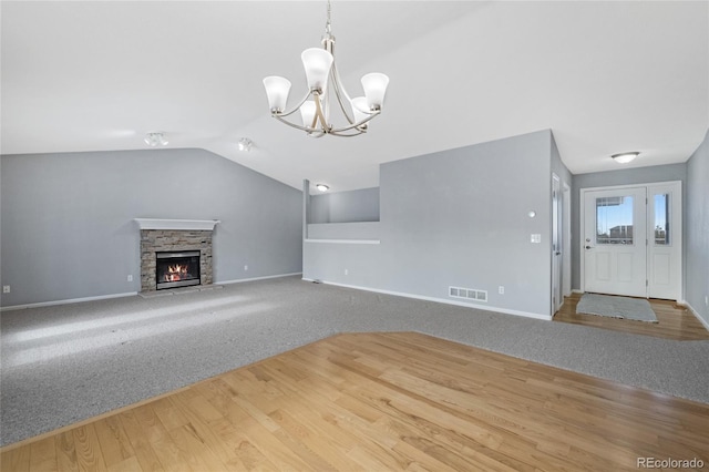 unfurnished living room with an inviting chandelier, a stone fireplace, vaulted ceiling, and carpet