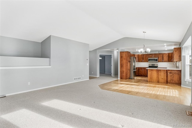 kitchen with vaulted ceiling, pendant lighting, sink, a notable chandelier, and stainless steel appliances