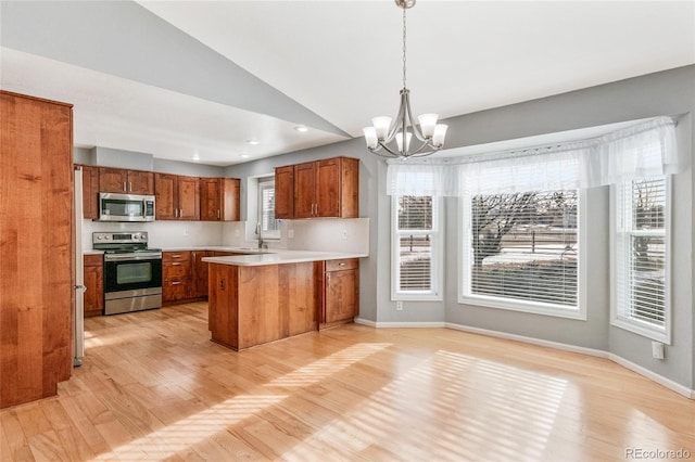 kitchen with decorative light fixtures, sink, kitchen peninsula, stainless steel appliances, and light hardwood / wood-style flooring