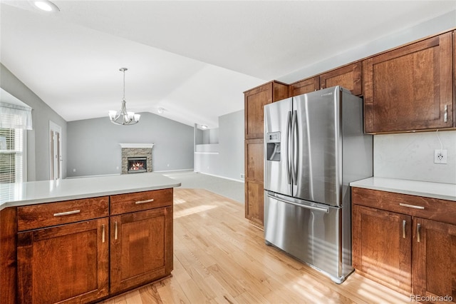 kitchen with vaulted ceiling, pendant lighting, a fireplace, stainless steel fridge, and light hardwood / wood-style floors