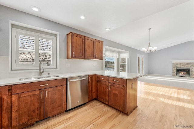 kitchen featuring a sink, stainless steel dishwasher, a peninsula, a stone fireplace, and lofted ceiling