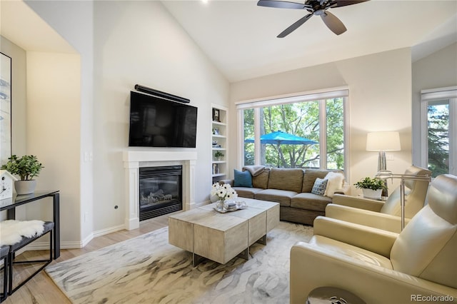 74 Blue Heron Dr, Greenwood Village, CO 80121 - living area with light wood-style flooring, built in shelves, ceiling fan, a glass covered fireplace, and high vaulted ceiling