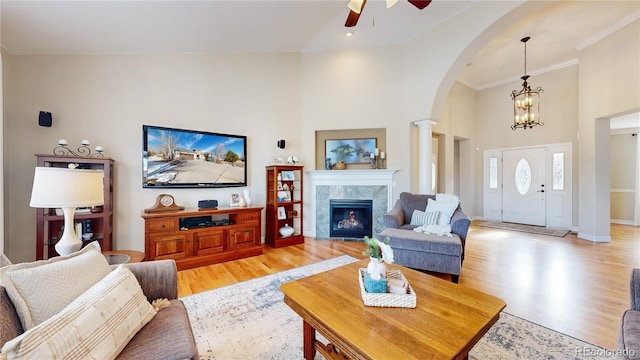 living room with ceiling fan with notable chandelier, decorative columns, a tiled fireplace, a high ceiling, and light wood-type flooring