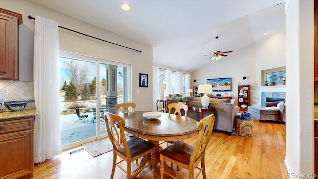 dining area with lofted ceiling, a tile fireplace, light hardwood / wood-style floors, and ceiling fan