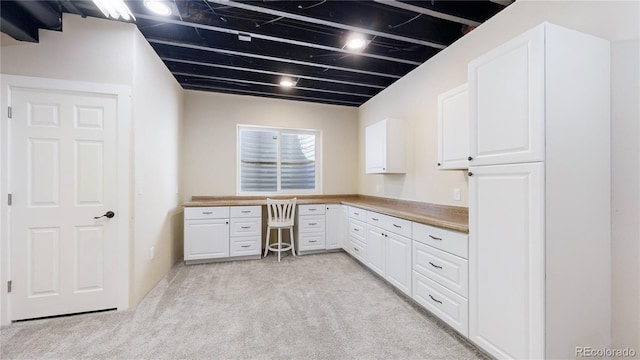 kitchen with white cabinetry, light carpet, and built in desk