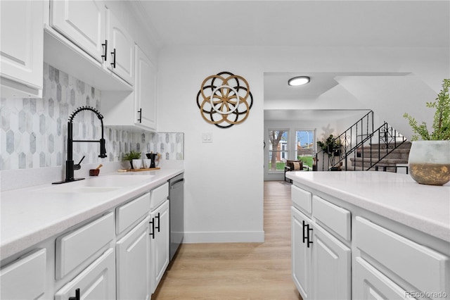 kitchen featuring a sink, baseboards, white cabinets, light countertops, and light wood-style flooring