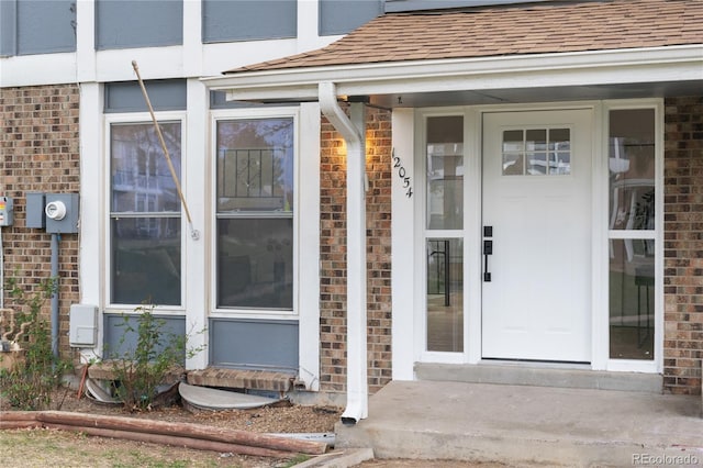 view of exterior entry with brick siding and a shingled roof