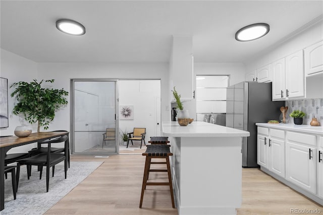 kitchen featuring tasteful backsplash, a breakfast bar area, light countertops, white cabinetry, and light wood-type flooring