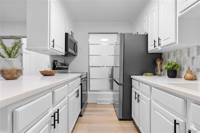kitchen with white cabinets, light countertops, light wood-style flooring, stainless steel appliances, and backsplash