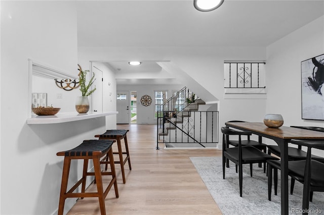 dining space featuring light wood-type flooring, a raised ceiling, baseboards, and stairway