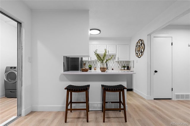 kitchen with a kitchen bar, washer / clothes dryer, fridge, white cabinetry, and light wood-style flooring