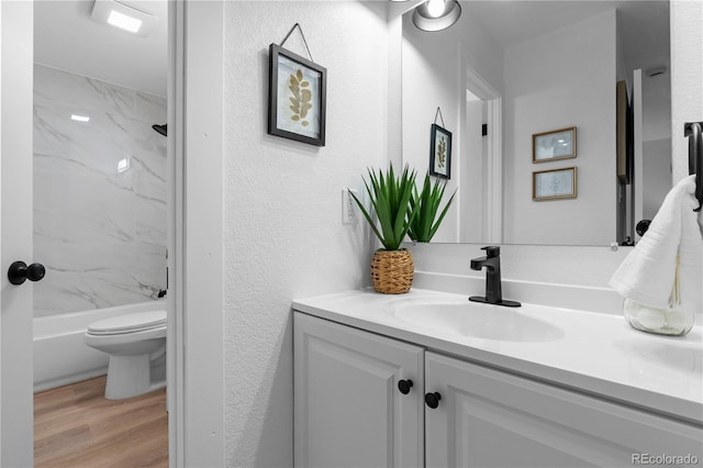 full bath with vanity, a textured wall, shower / bathtub combination, wood finished floors, and toilet