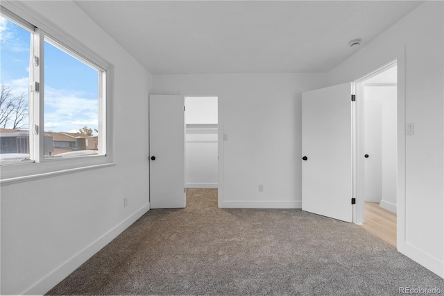 unfurnished bedroom featuring carpet flooring, baseboards, and a walk in closet