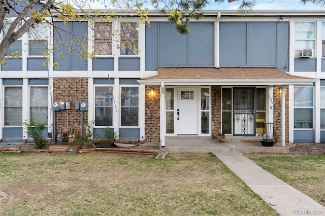 view of property with a porch, brick siding, and a front lawn