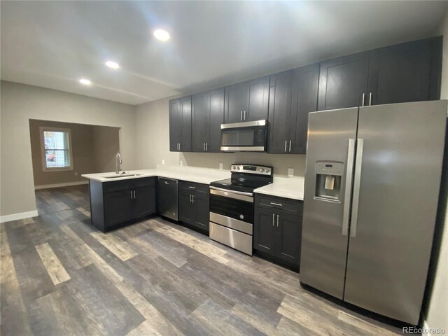 kitchen with appliances with stainless steel finishes, wood-type flooring, kitchen peninsula, and sink