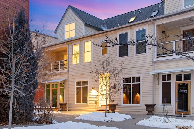 snow covered property with entry steps, a shingled roof, and a balcony