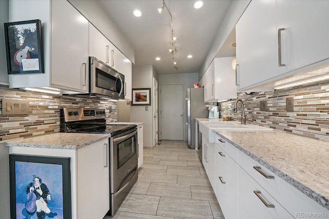 kitchen with decorative backsplash, white cabinets, light stone counters, a sink, and appliances with stainless steel finishes