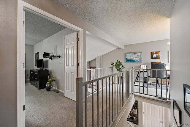 hallway featuring baseboards, carpet, a textured ceiling, and an upstairs landing