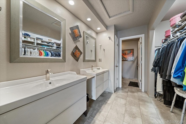 bathroom with a sink, a textured ceiling, recessed lighting, baseboards, and two vanities