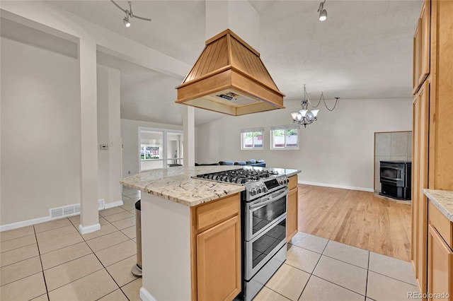 5722 W Chestnut Ave, Littleton, CO 80128 - kitchen featuring double oven range, rail lighting, premium range hood, light tile patterned floors, and a wood stove