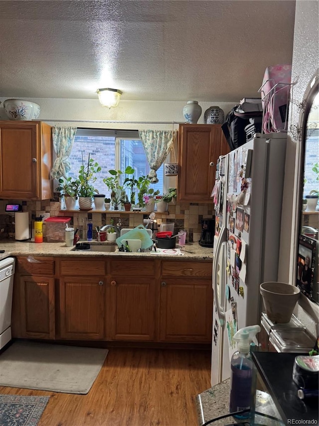 kitchen featuring backsplash, white appliances, a textured ceiling, and light wood-type flooring