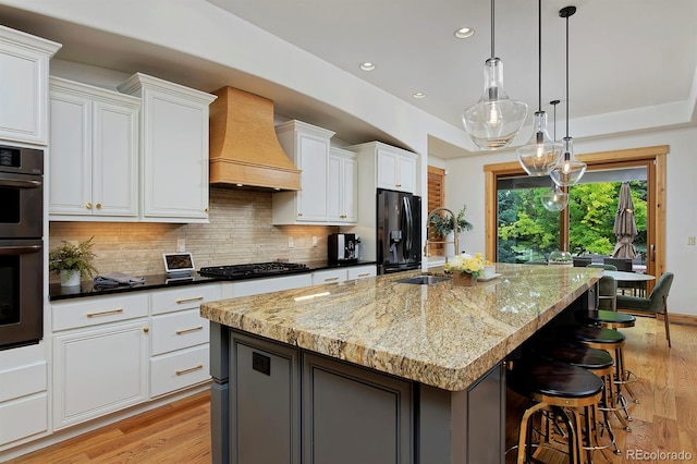 14370 Osage St, Westminster, CO 80023 - kitchen with custom range hood, light wood finished floors, refrigerator with ice dispenser, an island with sink, and recessed lighting
