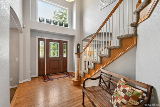 foyer with a healthy amount of sunlight, a high ceiling, arched walkways, and wood finished floors