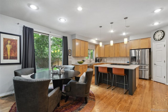 kitchen with light countertops, visible vents, light wood-style floors, a kitchen island, and stainless steel fridge with ice dispenser