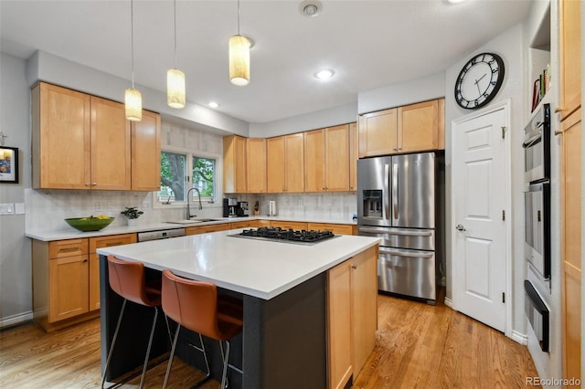 kitchen featuring light wood finished floors, light countertops, backsplash, appliances with stainless steel finishes, and a kitchen island