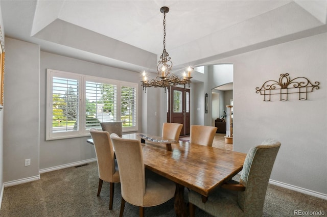 carpeted dining room featuring arched walkways, a tray ceiling, visible vents, an inviting chandelier, and baseboards