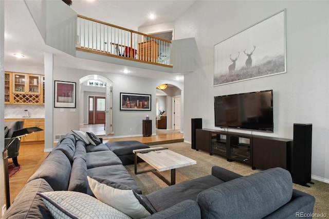 living room with arched walkways, light carpet, a high ceiling, baseboards, and a bar