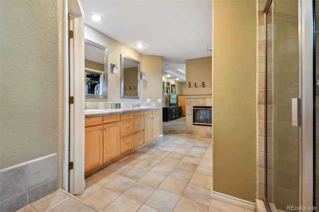 bathroom featuring double vanity, a tiled fireplace, a sink, a tile shower, and tile patterned floors