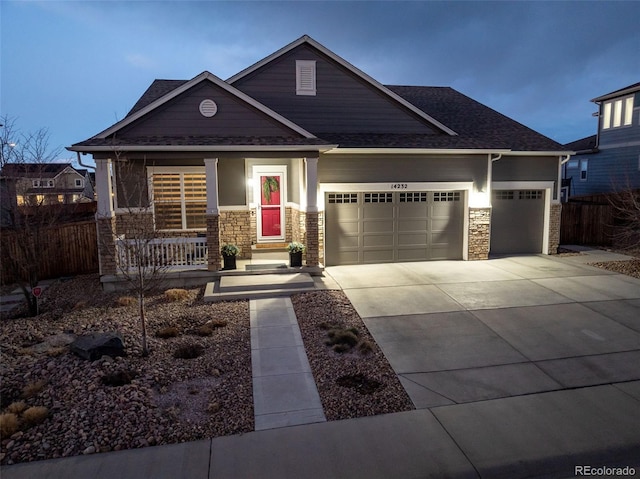 craftsman house featuring a garage, stone siding, driveway, and fence