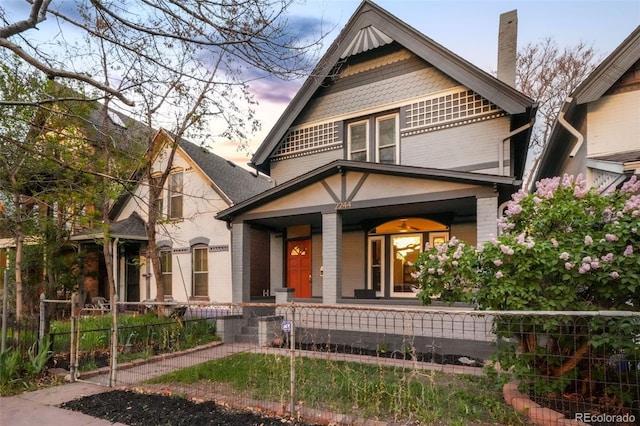 view of front of home featuring covered porch, a chimney, a fenced front yard, and brick siding