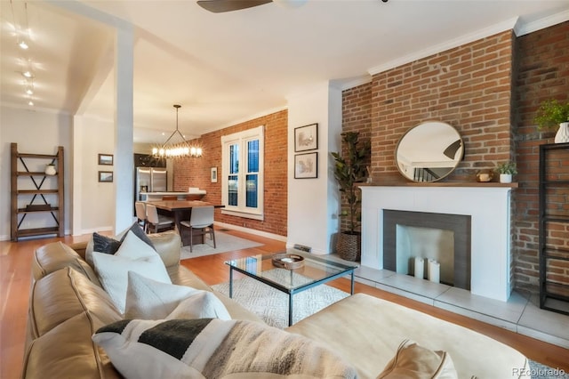 living room featuring baseboards, ceiling fan with notable chandelier, wood finished floors, and brick wall