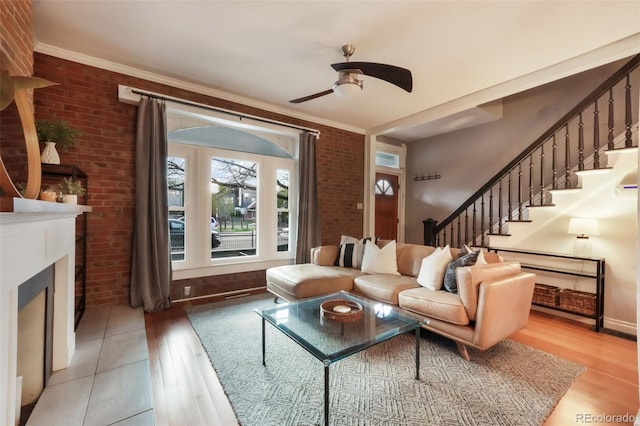 living area with light wood-style floors, a ceiling fan, stairs, and brick wall