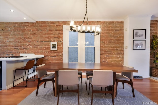 dining room with brick wall, wood finished floors, baseboards, an inviting chandelier, and ornamental molding