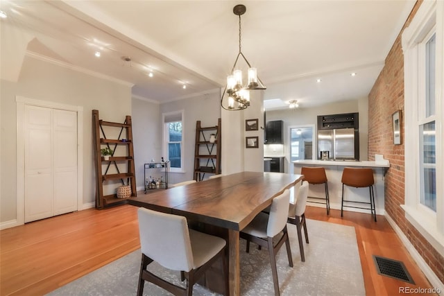 dining room featuring brick wall, visible vents, a chandelier, light wood-style floors, and ornamental molding