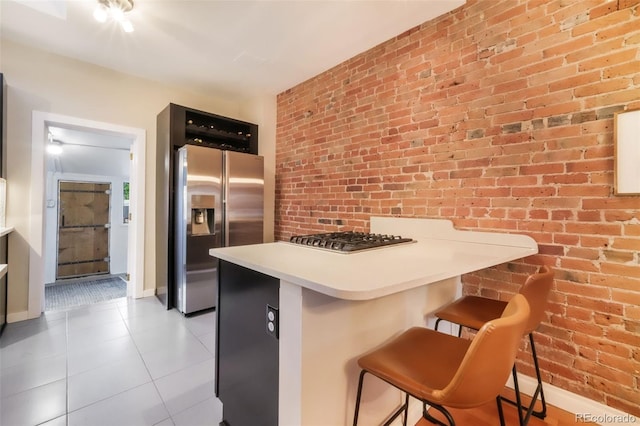 kitchen featuring a breakfast bar area, tile patterned floors, stainless steel appliances, baseboards, and a peninsula