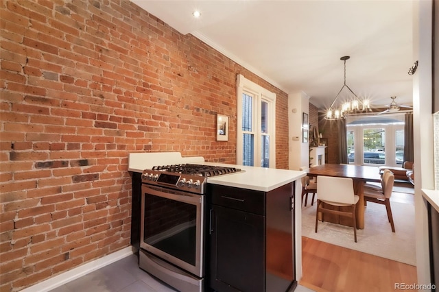 kitchen with light countertops, dark cabinetry, brick wall, a chandelier, and gas range