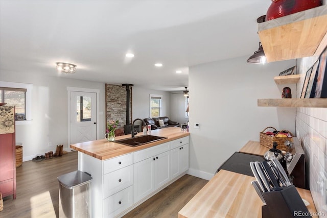 kitchen with a fireplace, white cabinetry, sink, wooden counters, and dark wood-type flooring