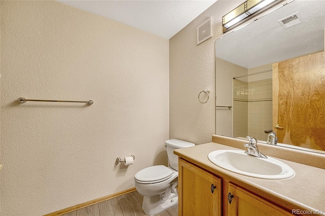 bathroom with a textured ceiling, hardwood / wood-style flooring, toilet, tiled shower, and vanity