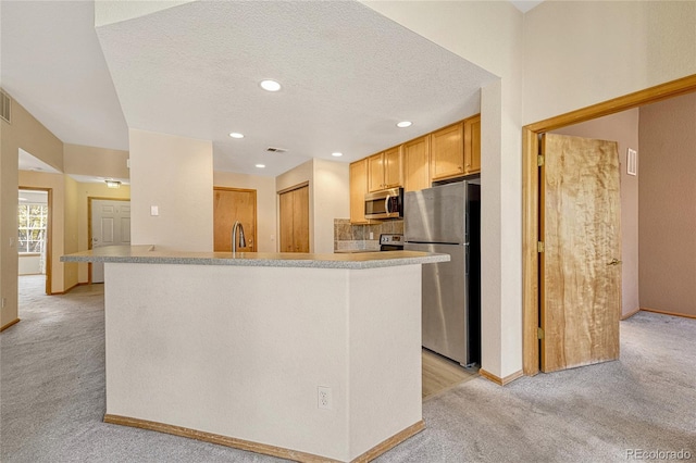 kitchen featuring light brown cabinetry, stainless steel appliances, a textured ceiling, and light colored carpet