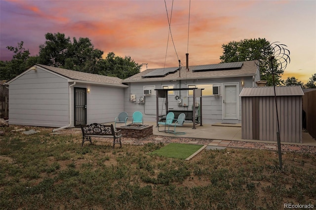 back of property at dusk featuring a storage shed, an outdoor fire pit, an outdoor structure, a patio area, and roof mounted solar panels