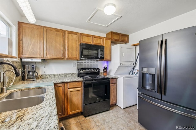 kitchen with stacked washer and clothes dryer, black appliances, sink, light tile patterned flooring, and light stone counters