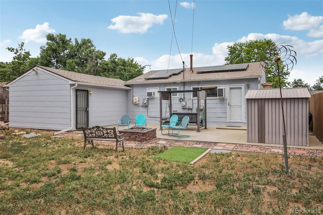 rear view of house featuring a lawn, an outdoor fire pit, solar panels, an outbuilding, and a patio