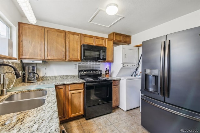 7940 Pontiac St, Commerce City, CO 80022 - kitchen featuring stacked washer and dryer, a sink, light tile patterned flooring, brown cabinetry, and black appliances